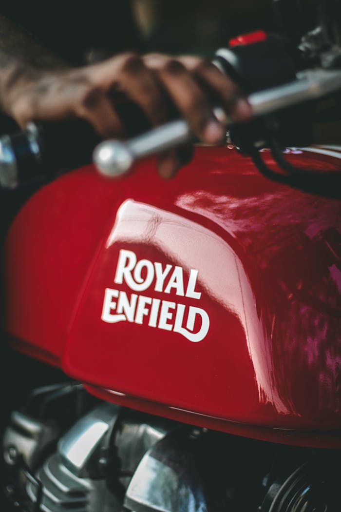 Detailed close-up of a red Royal Enfield motorcycle gas tank with a hand on the handlebar.